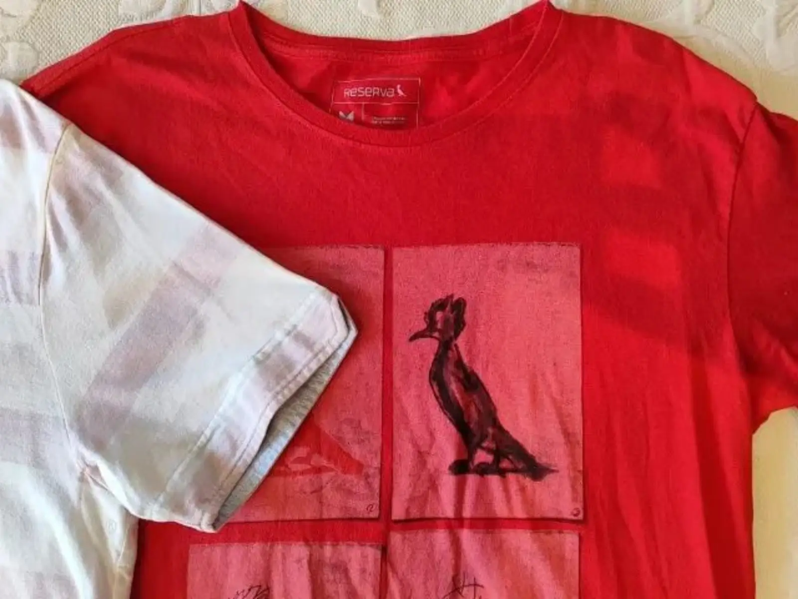 Close-up de uma camiseta vermelha da Reserva com a estampa do icônico pica-pau, símbolo da marca, disponível para compra com cupom de desconto.