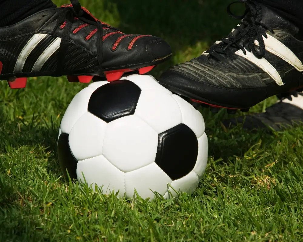 Duas chuteiras sobre uma bola de futebol no gramado, representando os artigos de futebol em oferta na Fut Fanatics.
