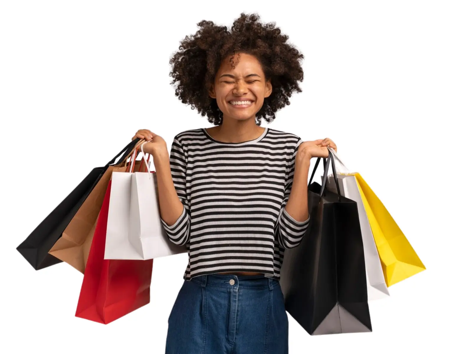 Uma jovem mulher negra com cabelo afro, vestindo uma blusa listrada e calça jeans, sorri de felicidade com os olhos fechados enquanto segura várias sacolas de compras coloridas em ambas as mãos, contra um fundo branco.