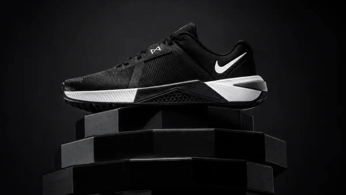 par de tenis nike metcon 10 em frente a uma barra de musculacao destacando a resistencia do cabedal